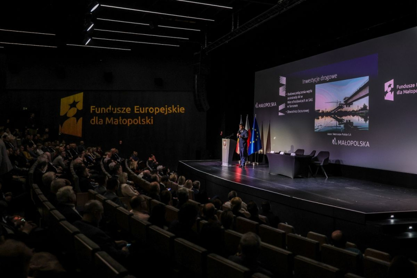 Widok na scenę podczas konferencji.  Na ekranie wyświetlana jest prezentacja.