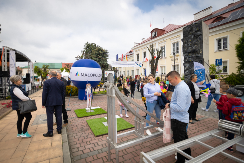Na pierwszym planie metalowe urządzenia, przy których stoi kilka osób. Na dalszym planie ścianka wspinaczkowa, balon reklamowy z napisem „Małopolska” oraz scena z zadaszeniem.