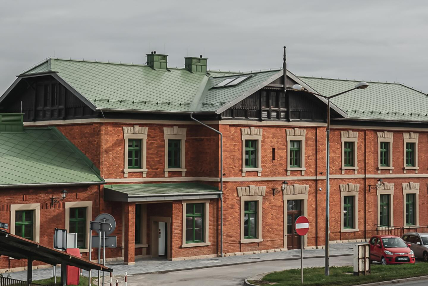 Budynek dworca PKP w Wadowicach. Budynek jest z czerwonej cegły i pokryty jest dachem z jasno zielonej blachy.