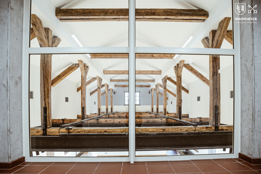 Poddasze budynku dworca PKP widoczne przez okno. Konstrukcja z drewninaych belek, biały sufit.