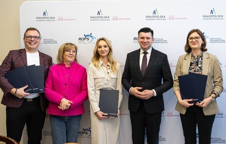 Uczestnicy wydarzenia stoją na tle ścianki z napisami Małopolska Ekonomia Społeczna.