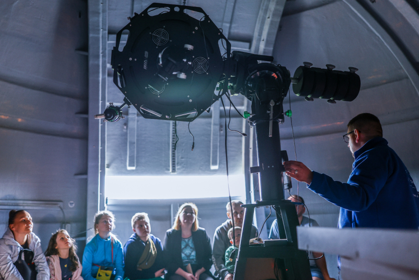 Mężczyzna, który jest astronomem pokazuje grupce osób instrument obserwacyjny w planetarium.