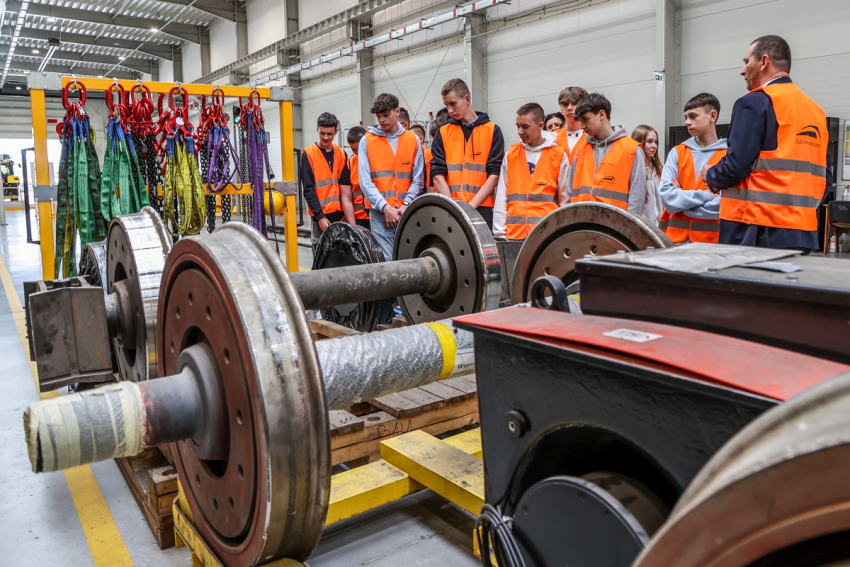 Grupa dzieci szkolnych i mężczyzna w pomieszczeniu obsługi taboru kolejowego.