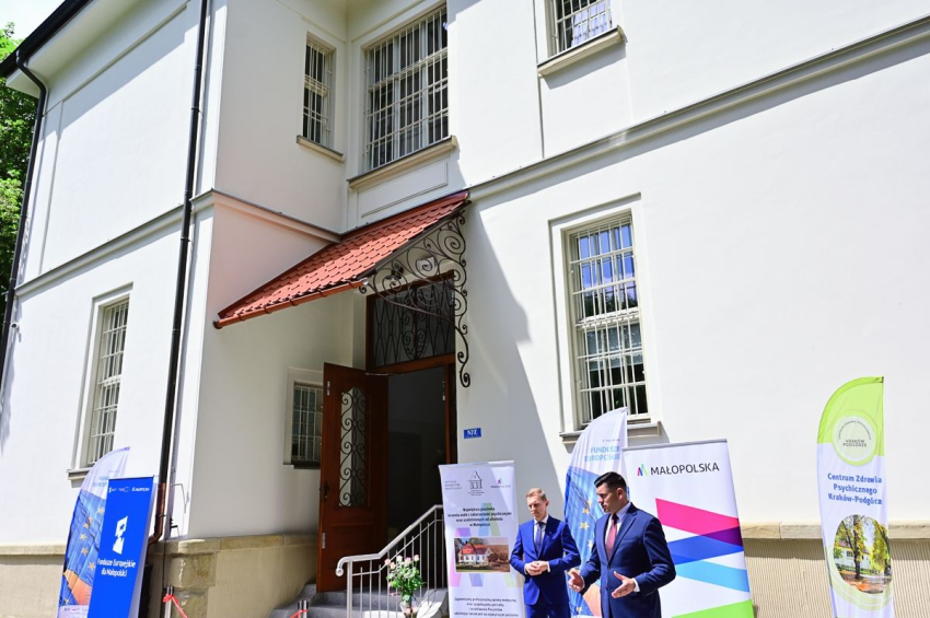 Dwóch mężczyzn w garniturach stojących przed budynkiem na terenie parku.