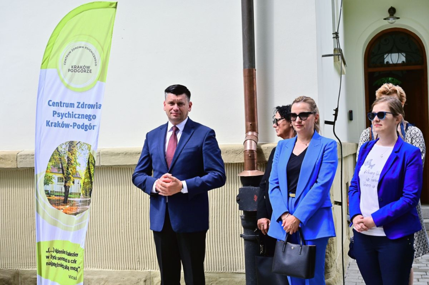 4 kobiety i jeden mężczyzna stoją przed budynkiem. Po lewej stronie winder z napisem Centrum Zdrowia Psychicznego Kraków Podgórze.