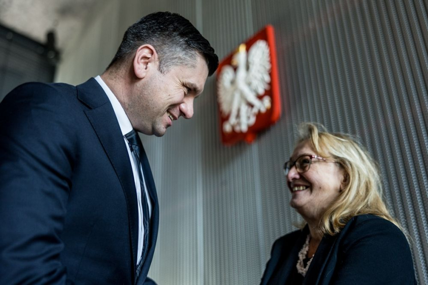 Uśmiechnięty elegancki mężczyzna rozmawia z elegancką kobietą.