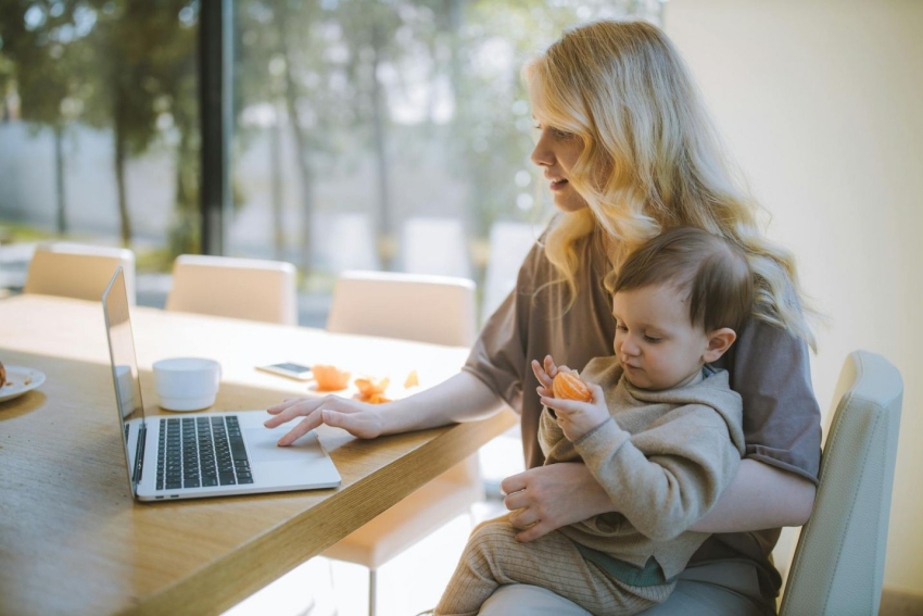 Mama pracująca przy laptopie siedzi z synkiem na kolanach