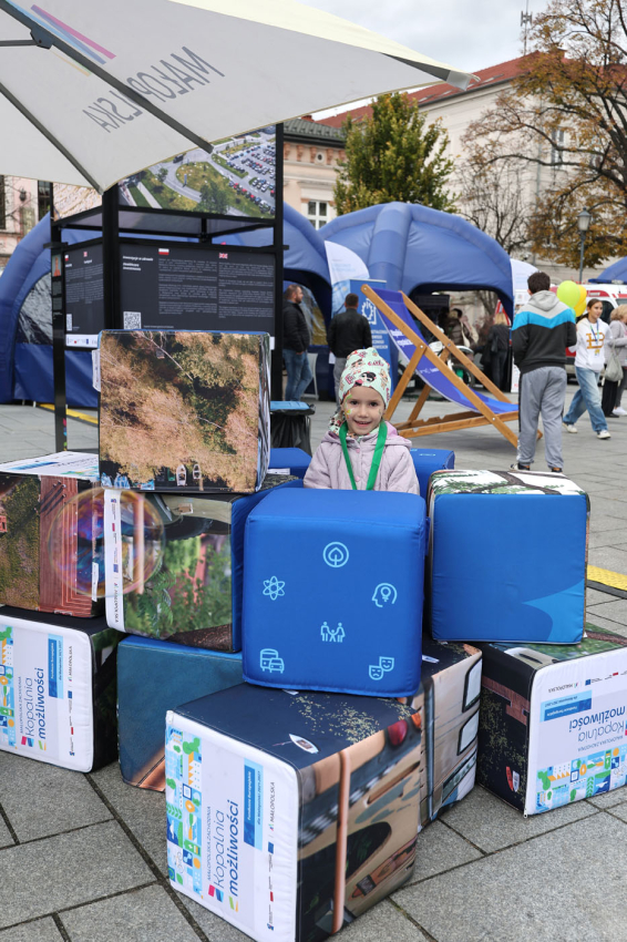 Mała dziewczynka stoi za pufami z logo wydarzenia.