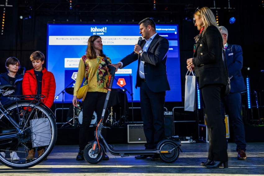 Marszałek Małopolski wręcza młodej dziewczynie, nagrodę w postaci hulajnogi.