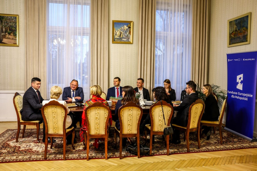 Uczestnicy spotkania siedzą i rozmawiaja przy stole.