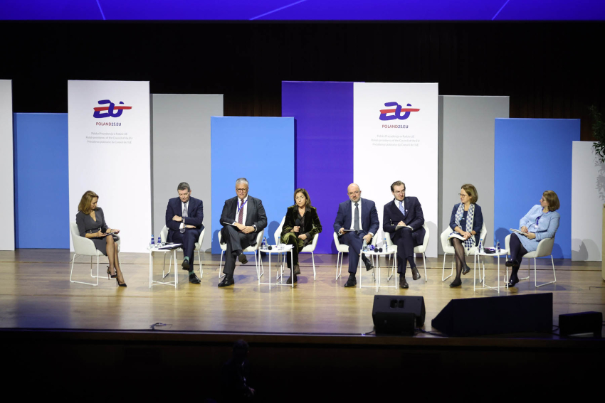 Osiem osób siedzących na krzesłach ustawionych obok siebie na scenie. W głębi kolorowe plasze z logotypem Polskiej prezydencji w Unii Eropejskiej w 2025 roku oraz adresem strony internetowej Poland25.EU