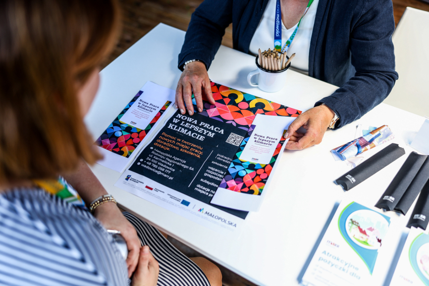 Pani z Małopolskiej Agencji Rozwoju Regionalnego udziela pokazuje ulotke z informacją Nowa Praca w lepszym klimacie