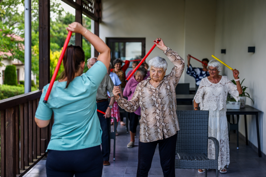 Seniorzy ćwiczą z trenerem na tarasie.