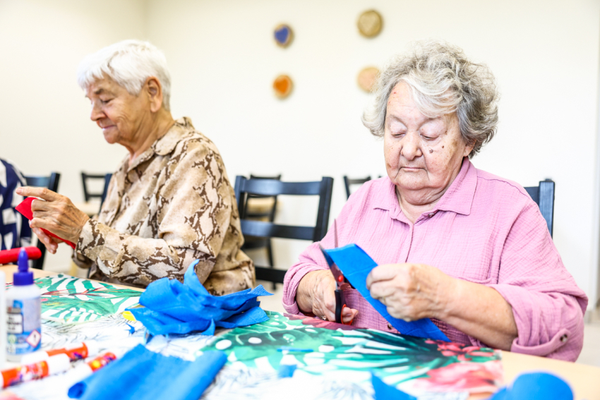 Seniorki biorą udział w warsztatach kreatywnych. Na stole bibuła, klej, kolorowe kartki.
