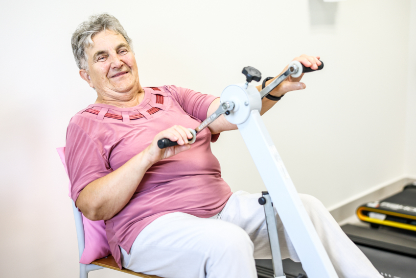 Seniorka ćwiczy na rowerku stacjonarnym.