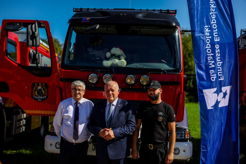 3ej mężczyźnie stoją przed wozem strażackim.