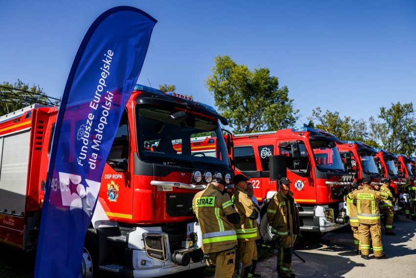 Strażacy przy samochodach strażackich.