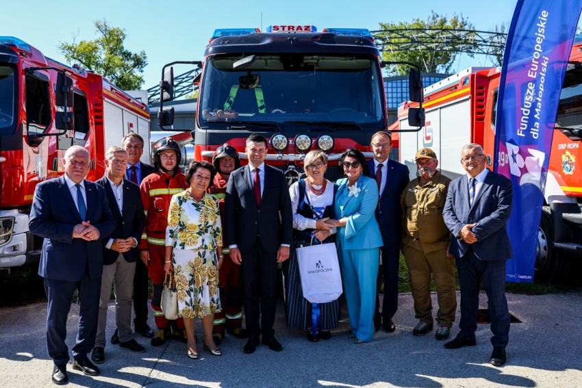 Zdjęcie grupowe uczestników wydarzenia na tle samochodu strażackiego.