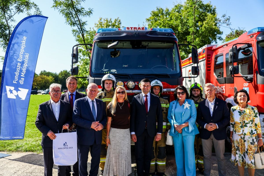 Zdjęcie grupowe uczestników wydarzenia na tle samochodu strażackiego.