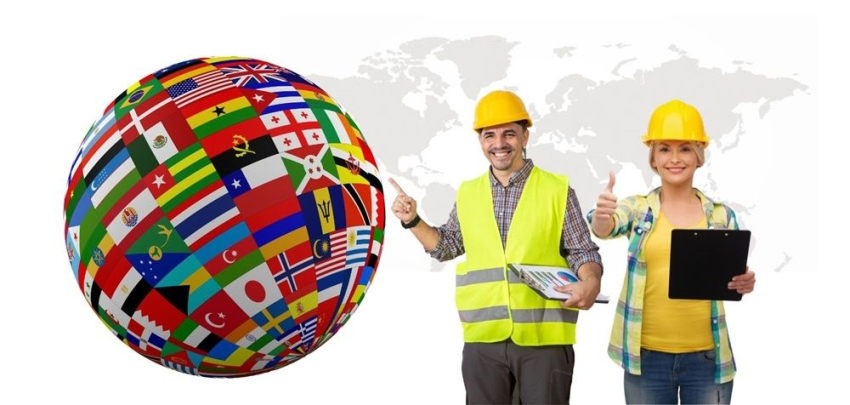 Kobieta i mężczyzna w żółtych hełmach roboczych wskazują na globus z flagami różnych krajów.