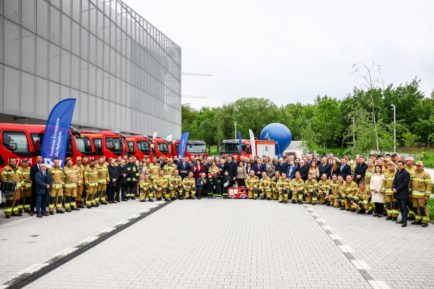 Zdjęcie grupowe uczestników wydarzenia. Za nimi samochody strażackie.