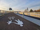Część mostu przeznaczona dla pieszych i rowerów. Namalowane białą farbą postacie osoby dorosłej i dziecka oraz rower.