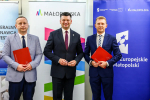 Marszałek Łukasz Smółka, Michał Tochowicz i przedstawiciel wykonawcy umowy prezentują podpisane dokumenty.