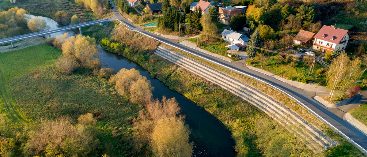 zabezpieczone osuwisko nad rzeką. Droga a przy niej domy mieszkalne