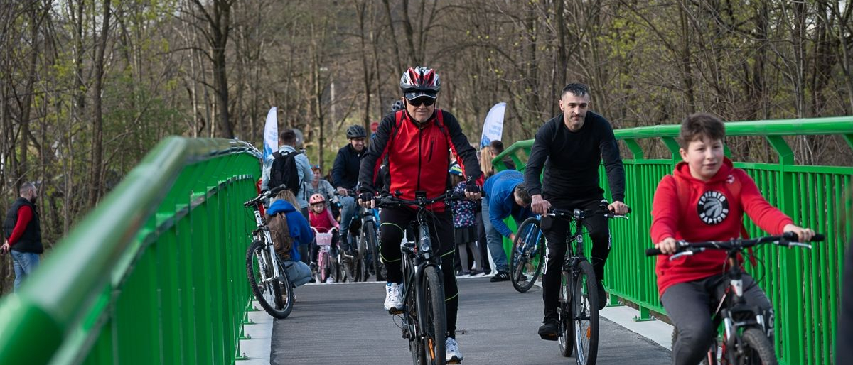 Grupa rowezrystów na kładce rowerowej. W tle widoczne drzewa