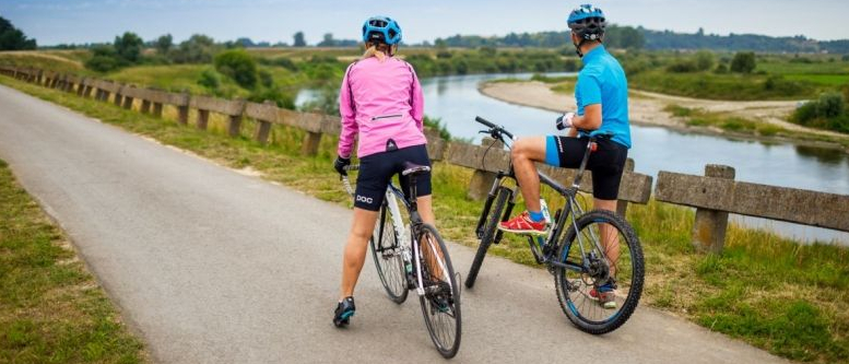 Dwoje rowerzystów, którzy przystanęli na ścieżce rowerowej i patrzą na nadrzeczny krajobraz