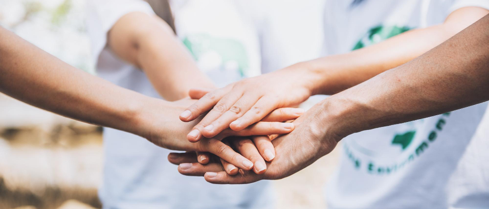 Dłonie kilku osób złożone jedne na drugich.