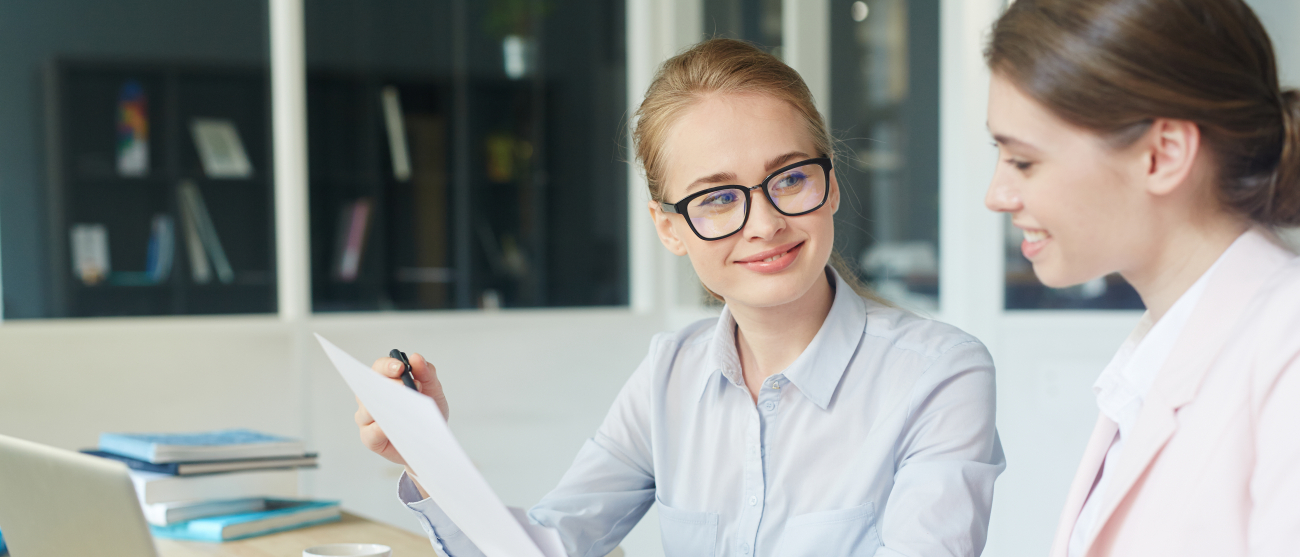 Dwie młode kobiety rozmawiają przy biurku.
