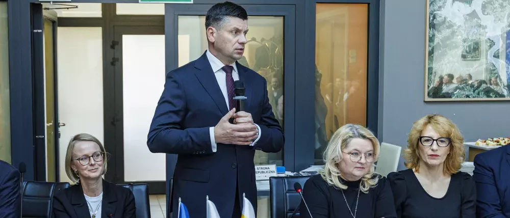 Marszałek Łukasz Smółka przemawia podczas posiedzenia Komitetu Monitorującego stojąc przy stole konferencyjnym, w otoczeniu uczestników wydarzenia