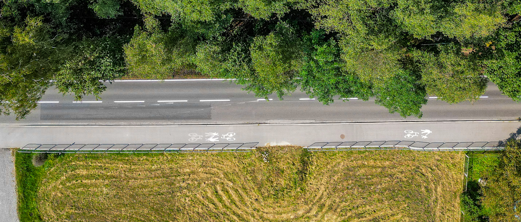 Widok z lotu ptaka na drogę i ciągnącą się wzdłuż niej ścieżkę pieszo-rowerową