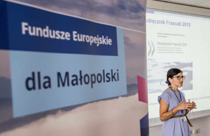 Roll-up z napisem Fundusz Europejskie dla Małopolski wystawiony obok prowadzącej szkolenie.